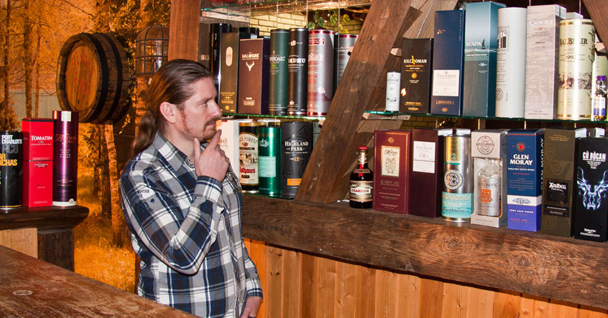 Mann steht vor einem Whiskyregal